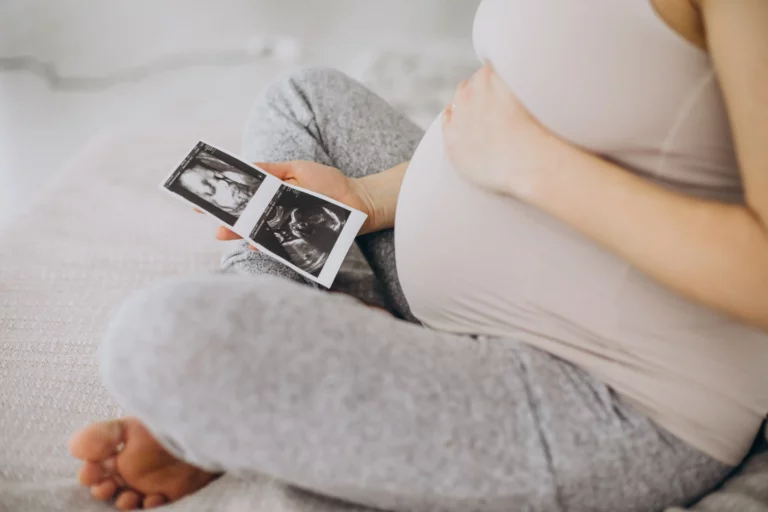 pregnant-woman-with-ultrasound-photo-sitting-bed-min